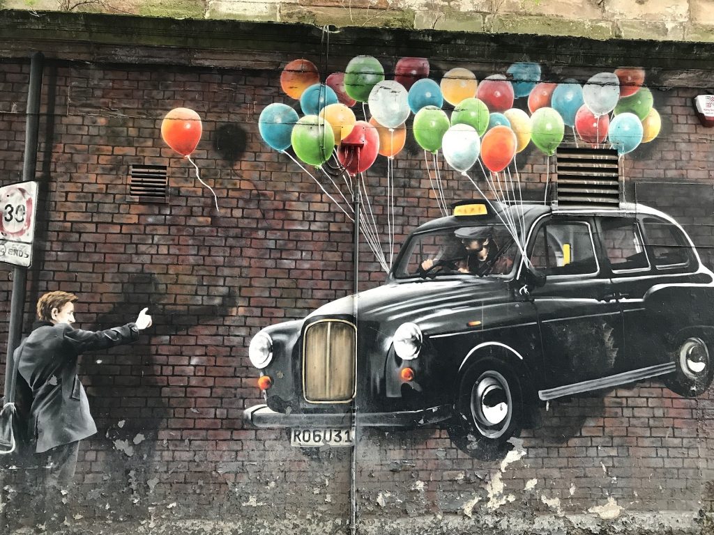 Schottland Sehenswürdigkeiten in Glasgow: Streetart an einer Backsteinmauer - ein Black Cab, das dank bunter Ballons in der Luft schwebt