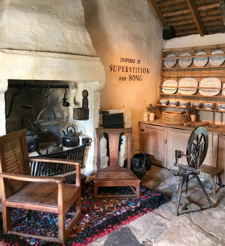 Zwei Holzstühle und ein Spinnrad vor dem Kamin im Cottage in Alloway in Ayrshire, in dem der Dichter Robert Burns geboren wurde