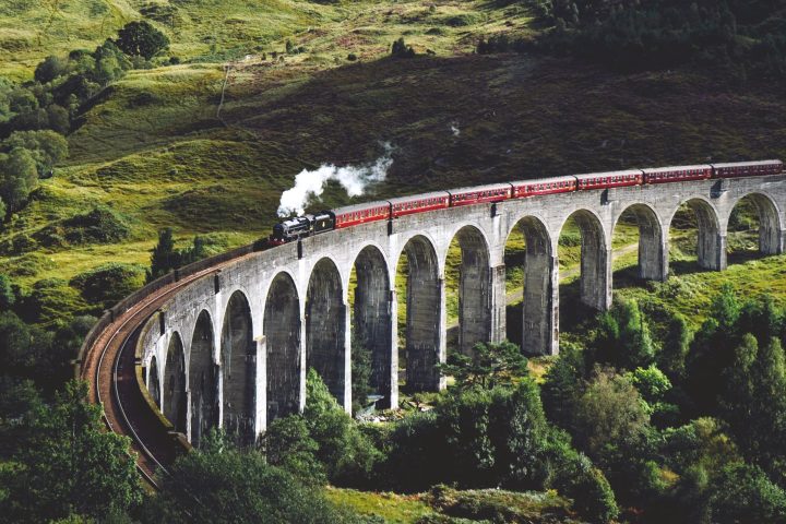 Schottland ohne Auto: Eine Dampflokomotive zieht einen Zug über eine steinerne Brücke in den schottischen Highlands