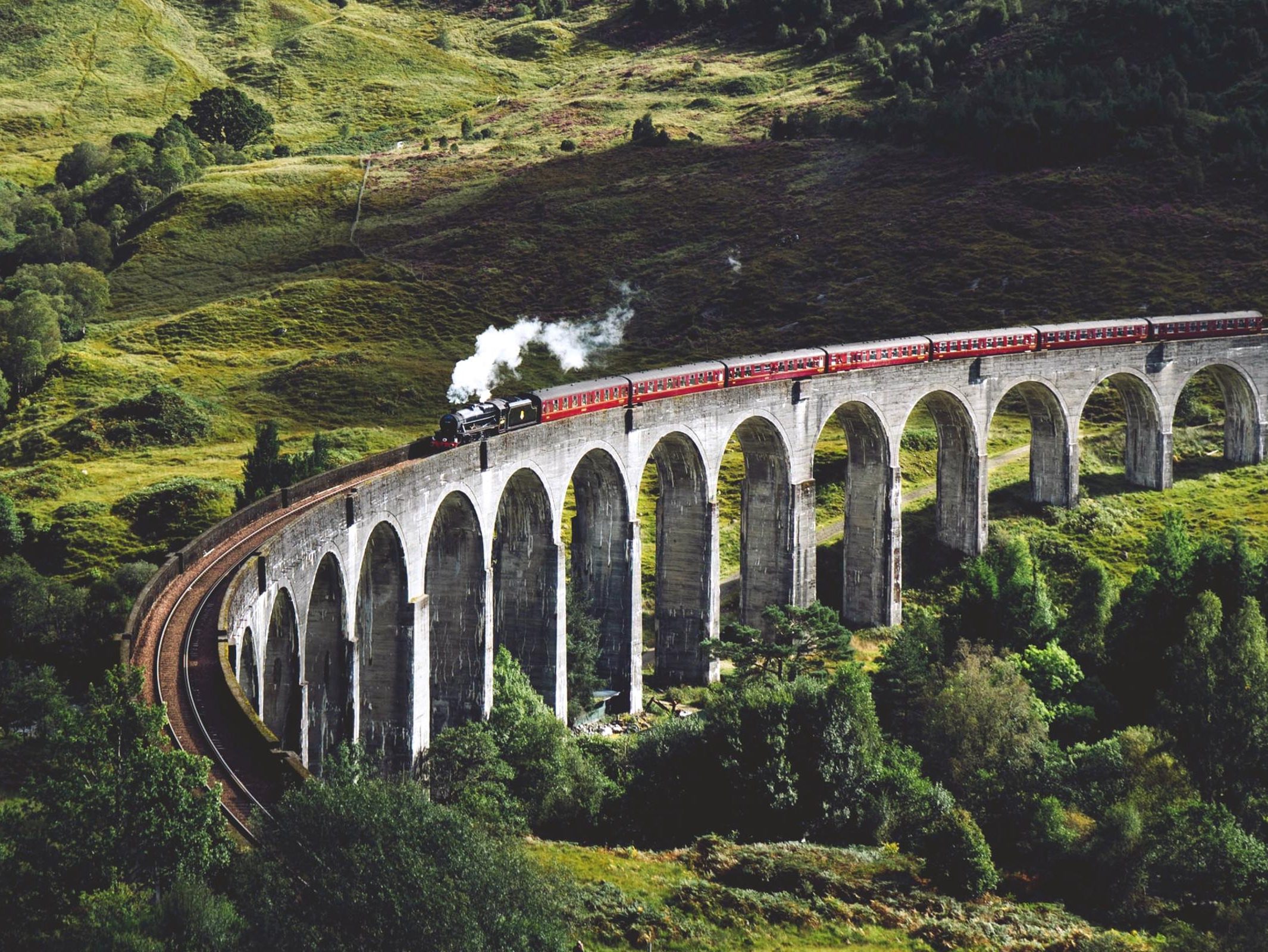 Schottland ohne Auto: Eine Dampflokomotive zieht einen Zug über eine steinerne Brücke in den schottischen Highlands